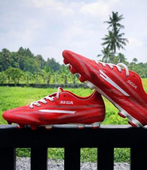 Red Sega Star football boots with white studs on a green background. 1